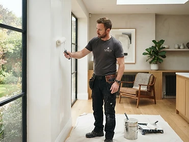 Handwerker streicht eine Wand in einem hellen Wohnraum